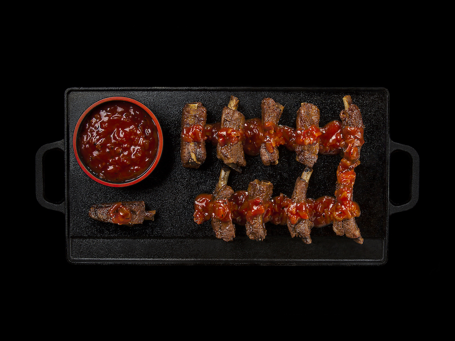 Coaste de porc caramelizate atent înșirate pe o tavă grill de fontă și garnisite cu un sos roșu barbecue.